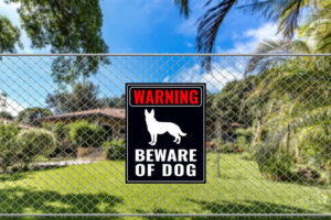 A Beware of Dog Sign on a fence near a bungalow house.